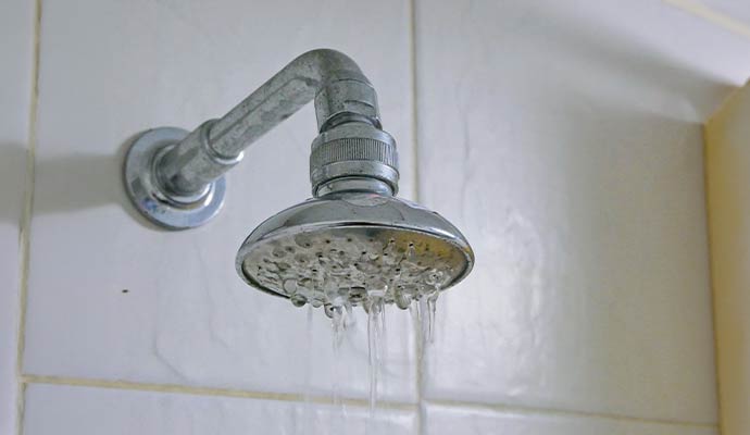 Old metal shower head leaking water from the nozzles