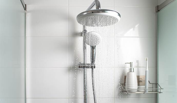 Rainfall shower head and handheld sprayer with water running in a white-tiled bathroom